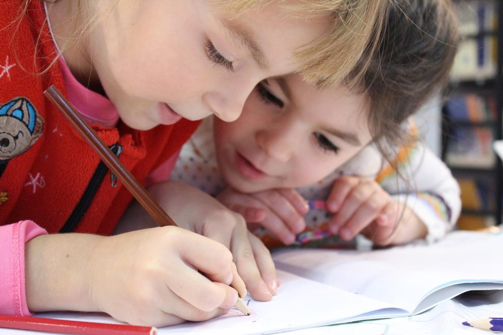 Two young children writing together in a notebook